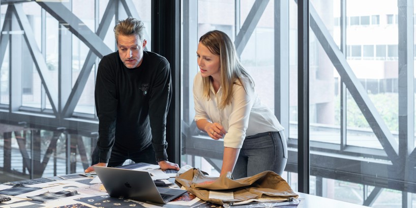 To stående kollegaer samarbejder ved bord med computer og dokumenter