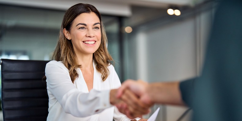 Smilende kvinde giver håndtryk over bord